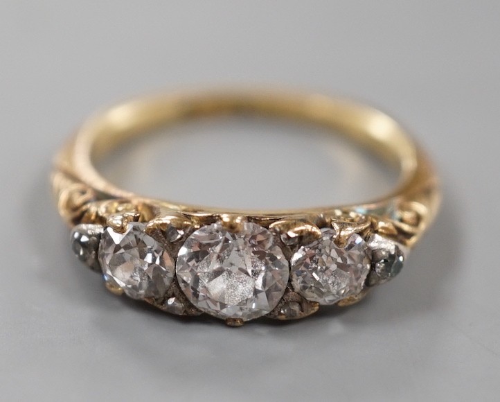 An early 20th century yellow metal and graduated three stone diamond ring, with diamond chip set shoulders, size J, gross weight 3 grams.